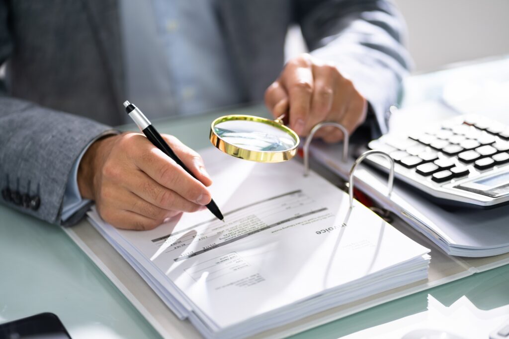 Person with an audit notice and a magnifying glass. Person is in a suit.