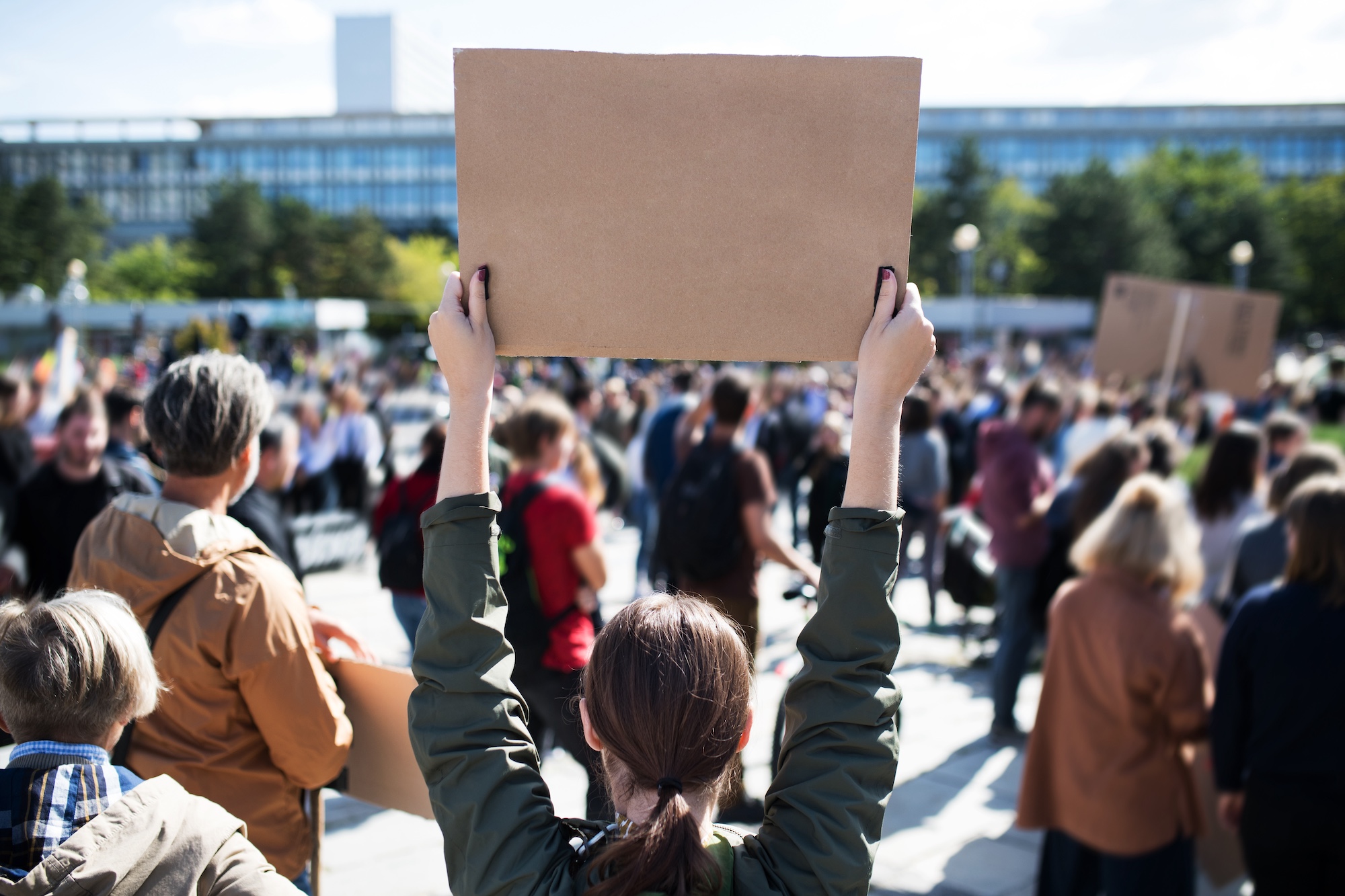 woman holding up a cardboard sign protesting with others outside