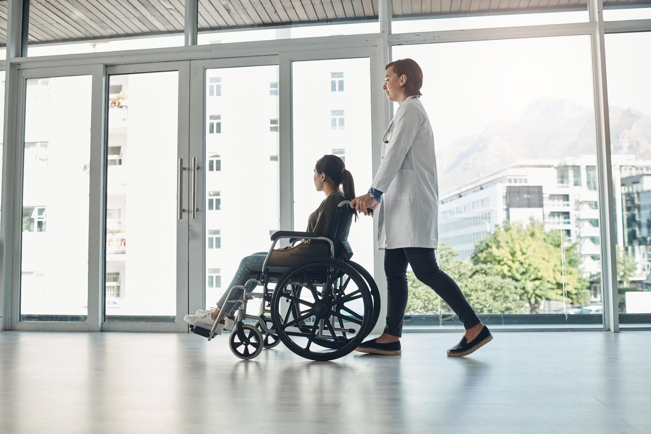 Doctor walking with patient in a wheelchair through hospital hallway